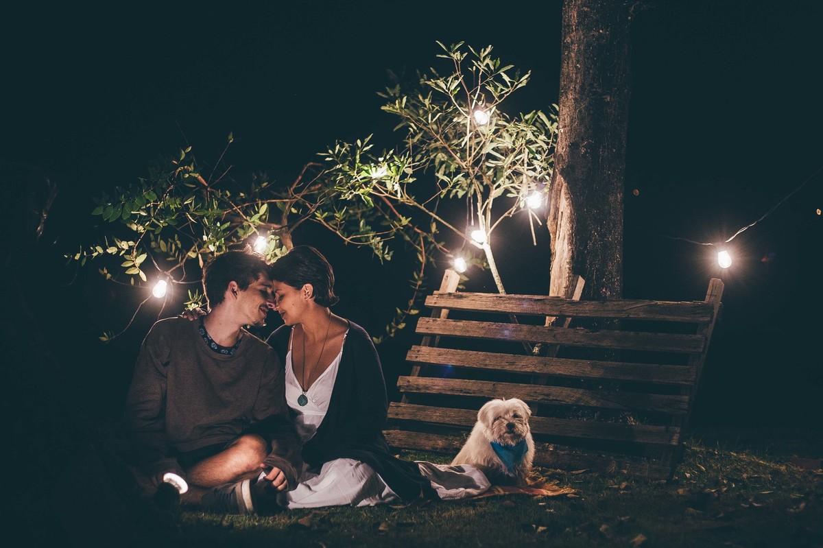 Foto de casal a noite com varal de luz, casal fazendo carinho um no outro e sorrindo