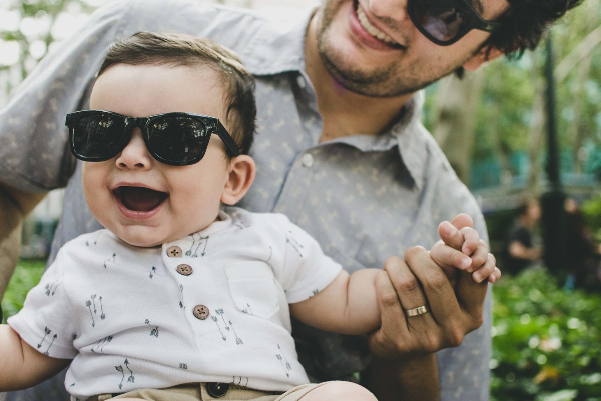 Ensaio fotográfico de família em Nova York, pai e filho com óculos escuro sorrindo, pai segurando filho no colo