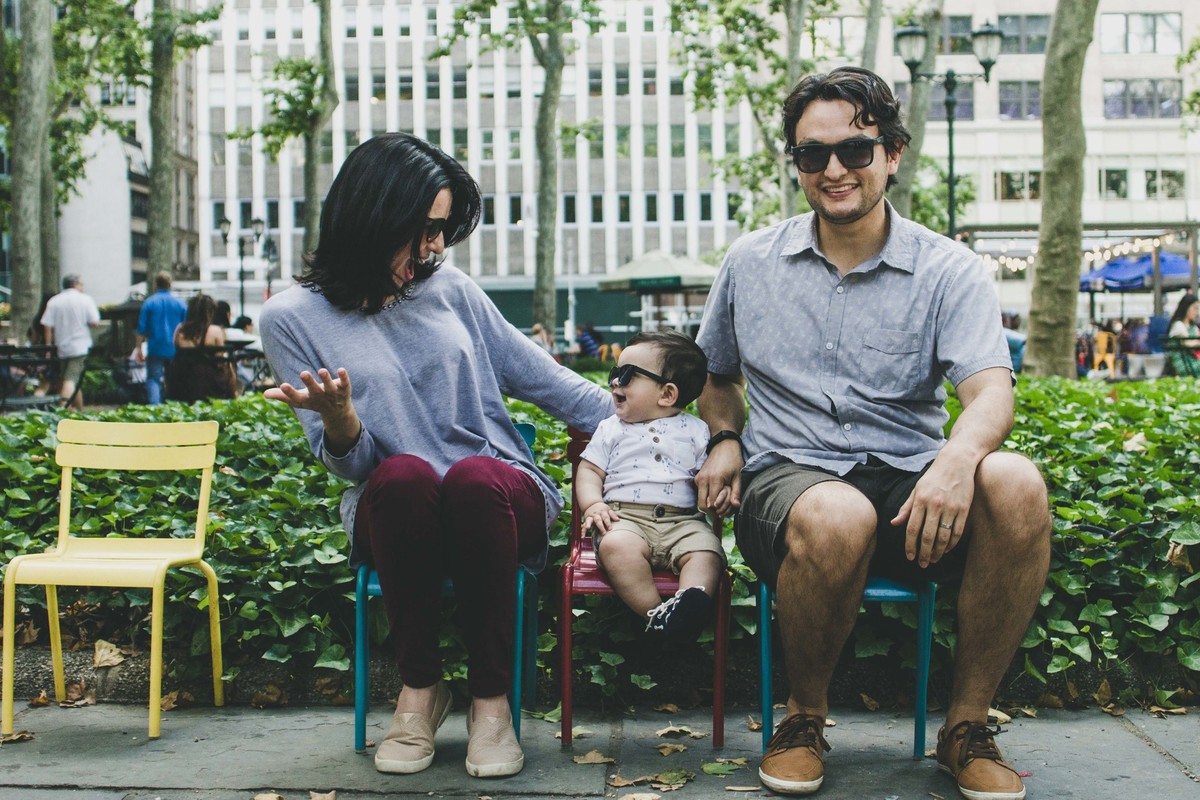 Ensaio fotográfico de família em Nova York, pai e mãe sentados ao lado do filho que posa e sorri para a mãe