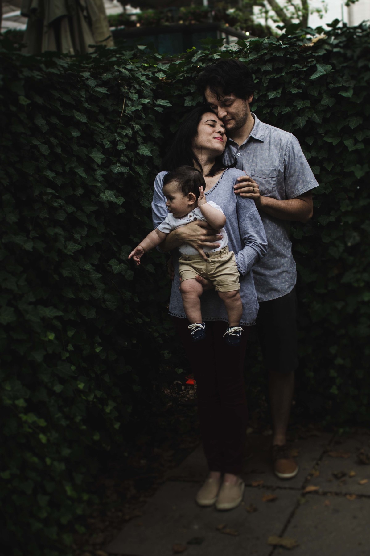 Ensaio fotográfico de família em Nova York, mãe segura filho no colo, pai abraça esposa, pai e mãe encostam as cabeças ,criança olha para o lado