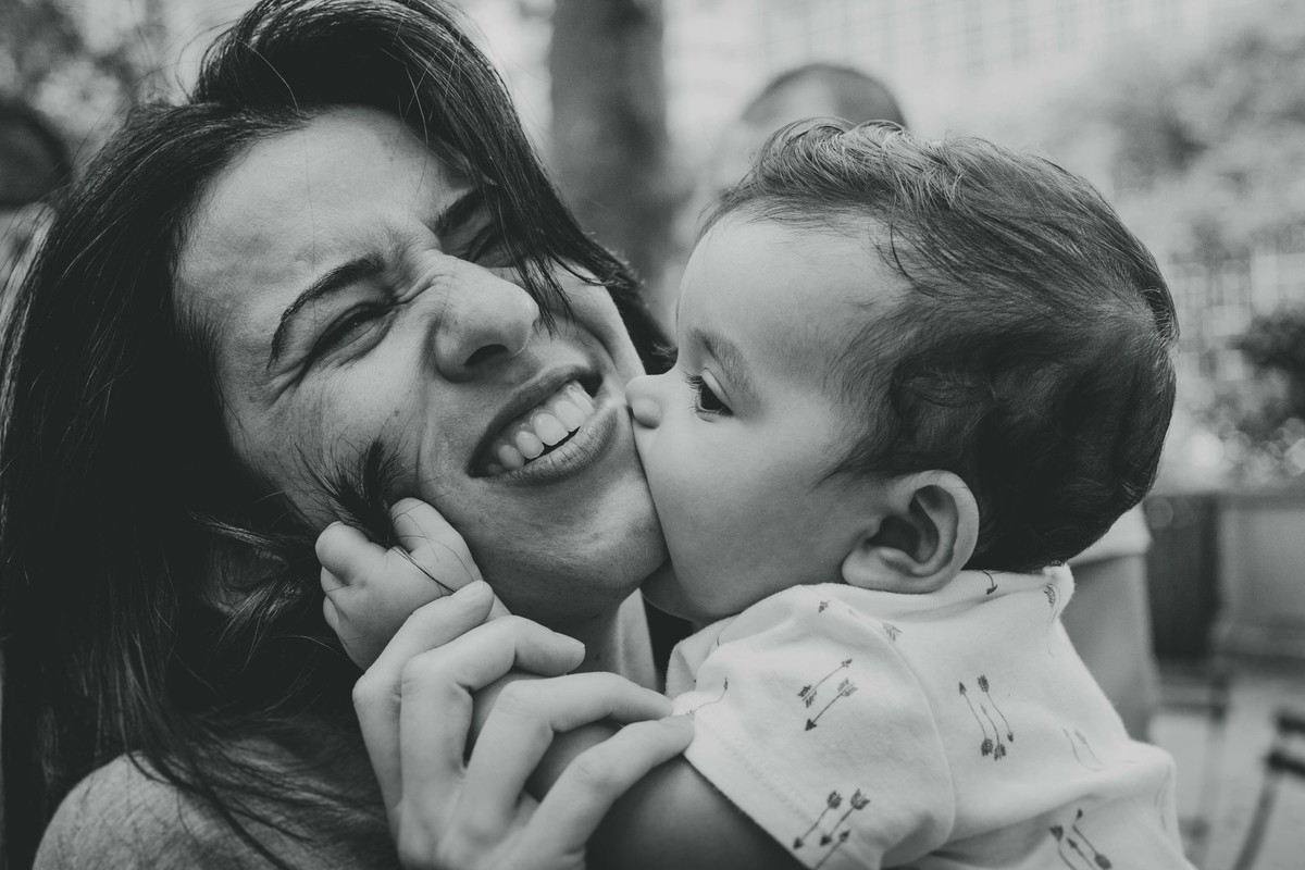 Ensaio fotográfico de família em Nova York, mãe segura filho no colo, filho morde mãe na bochecha, foto preto e branco