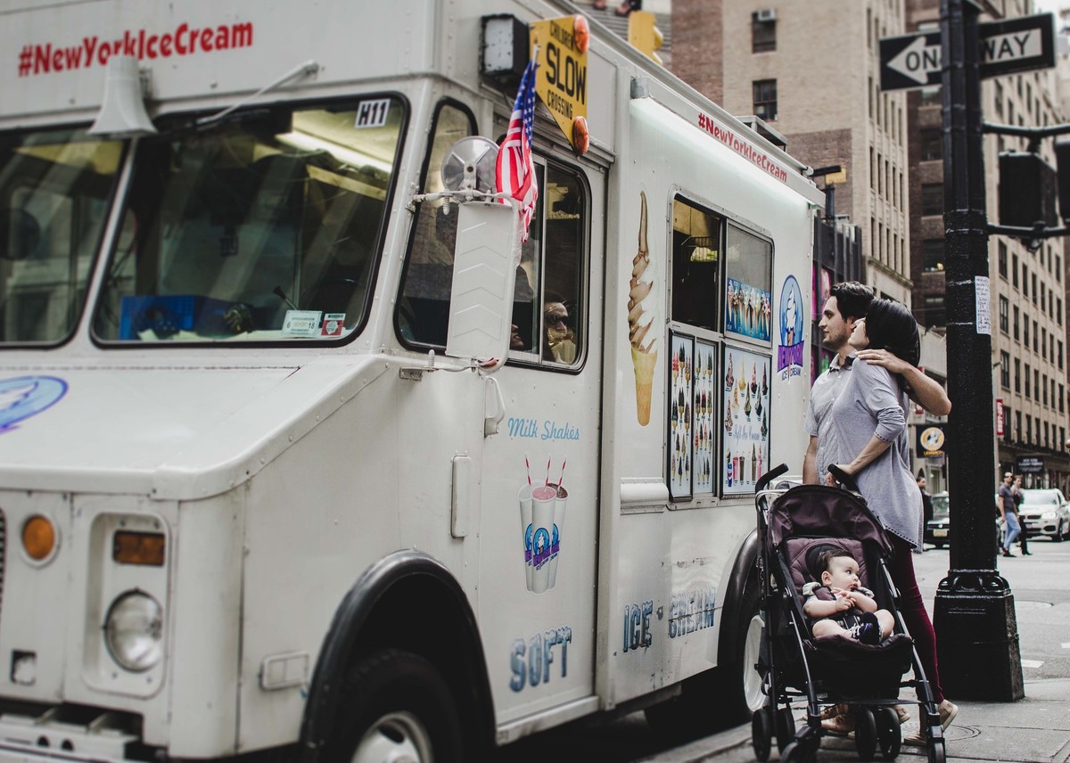 Ensaio fotográfico de família em Nova York, pai e mãe compram sorvete em um caminhão, eles estão em uma calçada de uma cidade grande