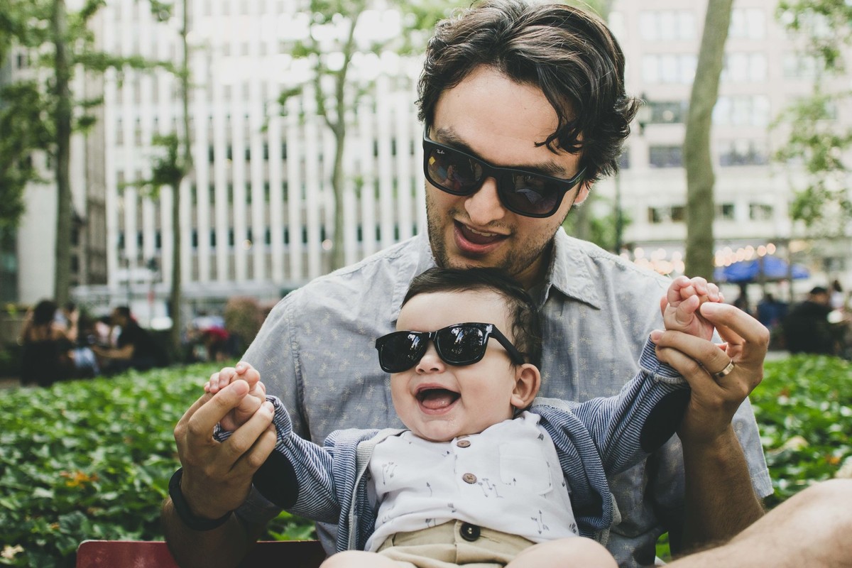 Ensaio fotográfico de família em Nova York, pai e filho com óculos escuro sorrindo, pai segurando filho no colo levantando os braços do filho