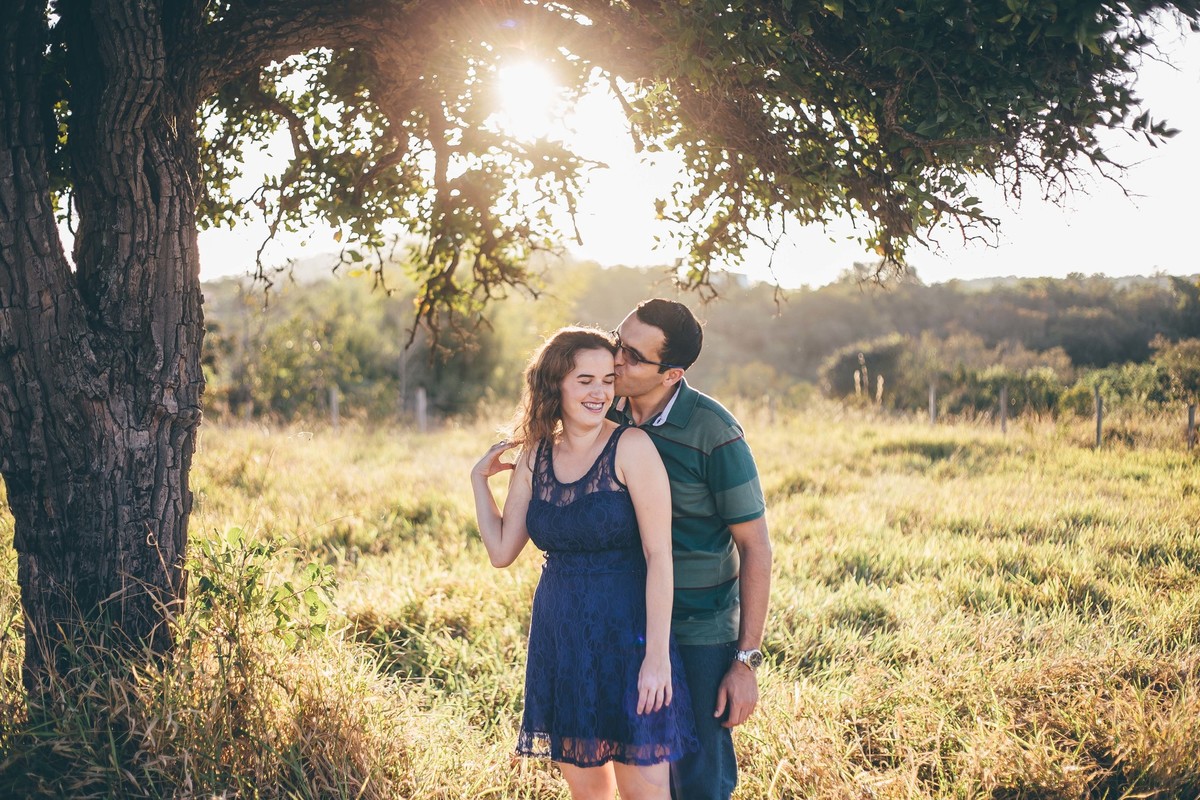 fotografia de casal no por do sol de baixo de uma arvore e no campo