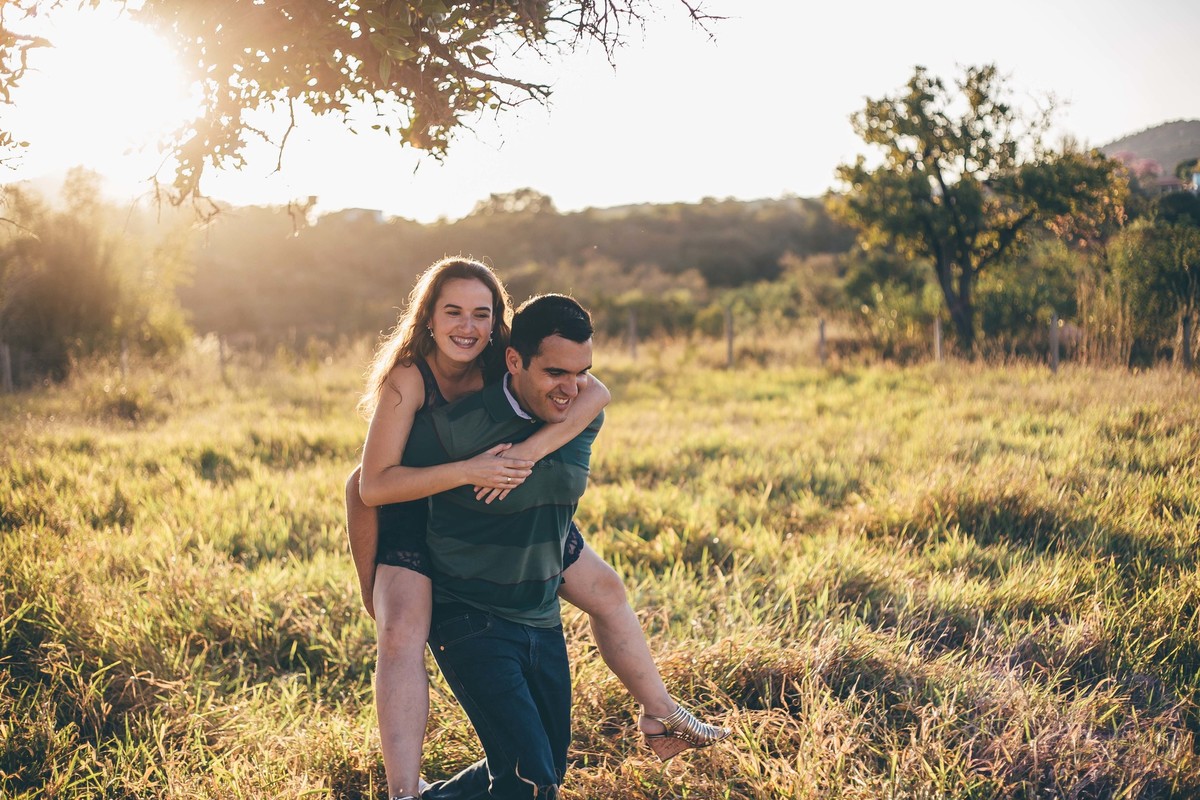 fotografia de casal no por do sol noiva andando de cavalinho no noivo no campo