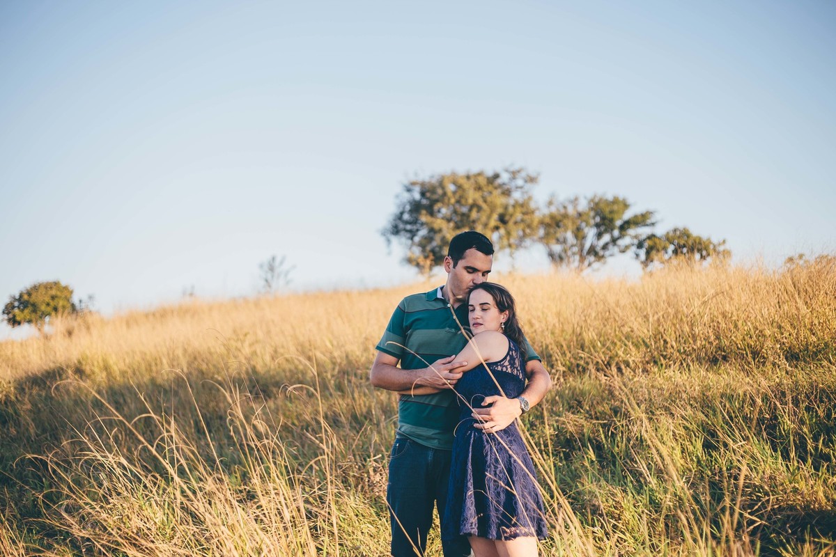 fotografia de casal no por do sol namorados se abraçando céu azul e mato seco