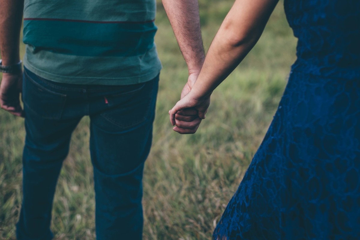 casal de mãos dadas caminhando no campo durante o por do sol
