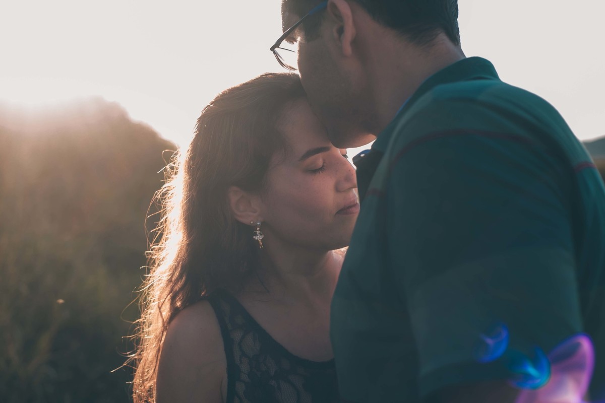 fotografia de casal no por do sol noivo beijando cabeça da noiva