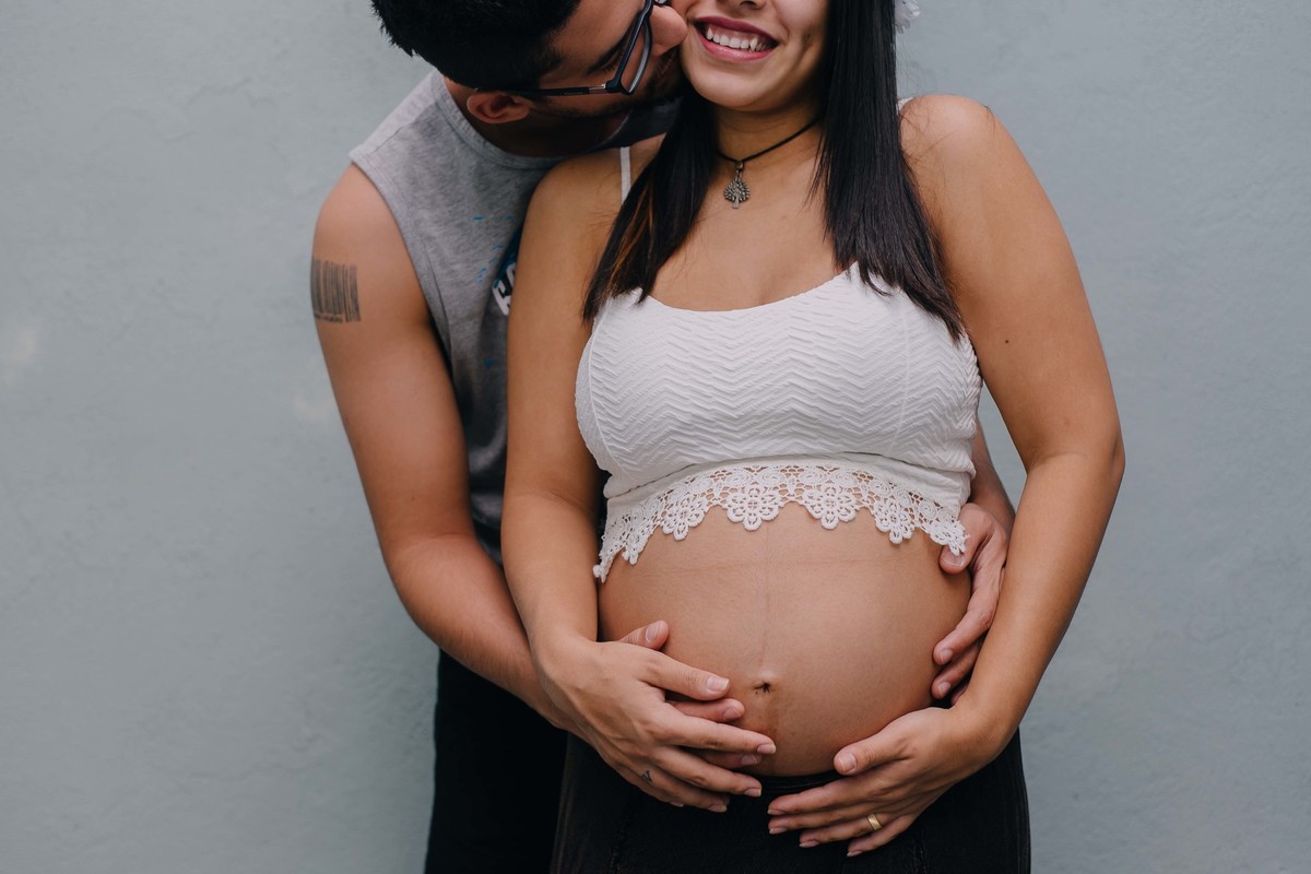 marido beijando a bochecha da esposa e abraçando ela por trás segurando sua barriga de grávida