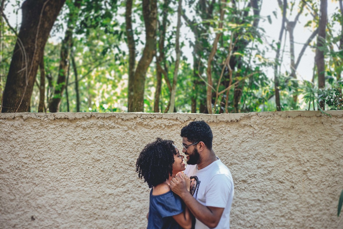 Ensaio de pré casamento em que o casal o está se olhando e segurando as mãos um do outro na frente de um muro