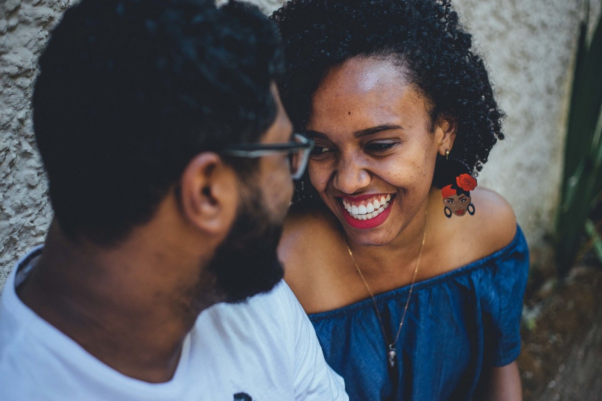 Noiva sorrindo com seus cabelos cacheados para o ensaio de casal usando um brinco com personalidade negra