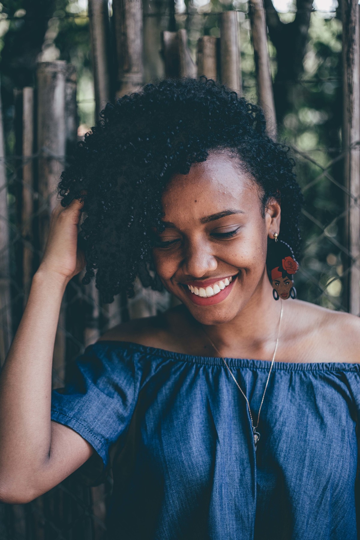 retrato feminino de mulher com cabelo cacheado e mexendo nele enquanto sorri pra foto