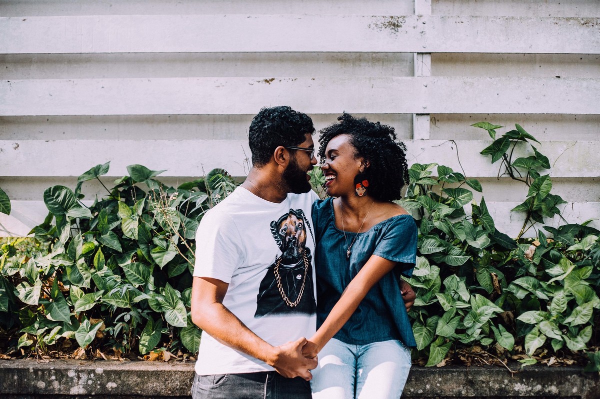 Noivos se olhando e sorrindo na frente de uma cerca de madeira