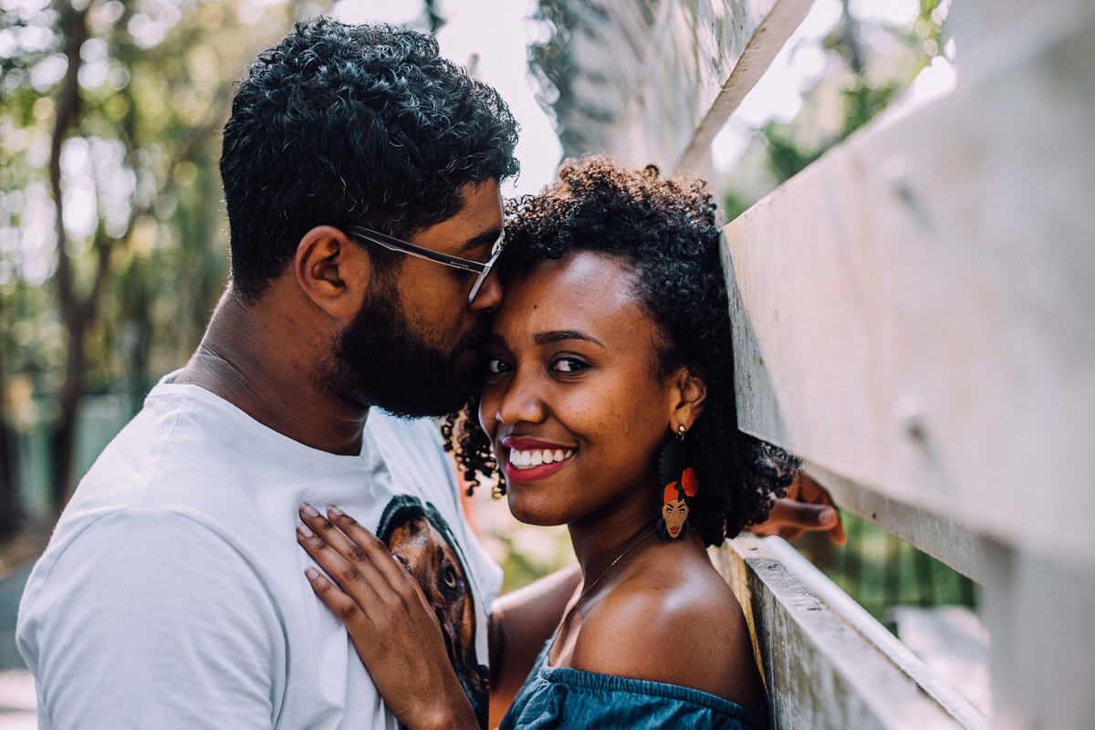 Noiva olhando para a camera repousando suas mãos sobre o peito do noivo enquanto ele beija sua testa
