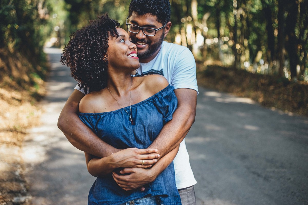 Noivos abraçados e olhando um para o outro e sorrindo em uma rua cheia de arvores de todos os lados