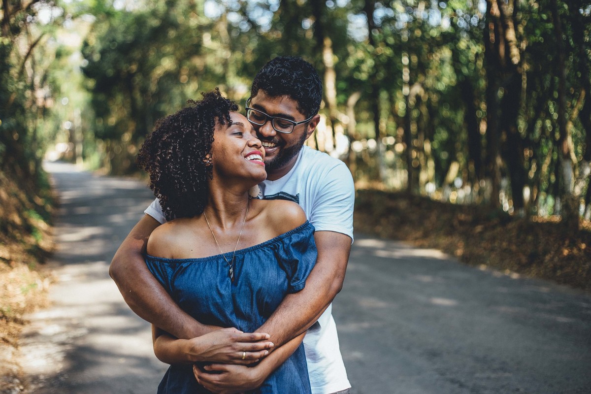 Noivos abraçados e olhando um para o outro e sorrindo em uma rua cheia de arvores de todos os lados