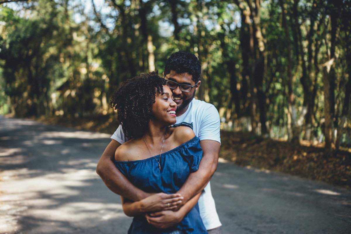 Noivos abraçados e olhando um para o outro e sorrindo em uma rua cheia de arvores de todos os lados