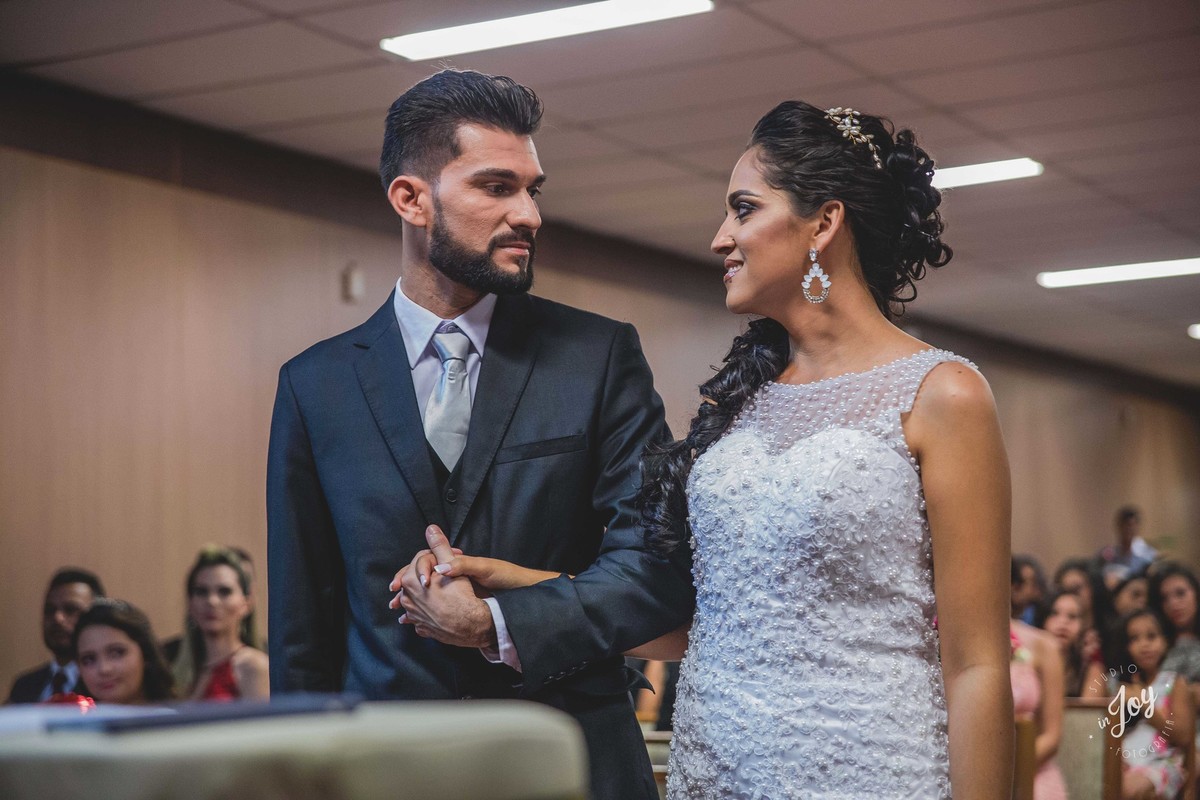 Noivos se olhando durante a cerimonia de casamento e a noiva sorri para o noivo enquanto ele segura a sua mão