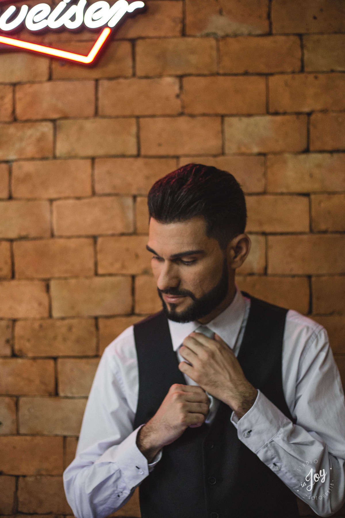 noivo ajustando a gravata na frete de uma parede de tijolinhos terminando de se arrumar para o casamento
