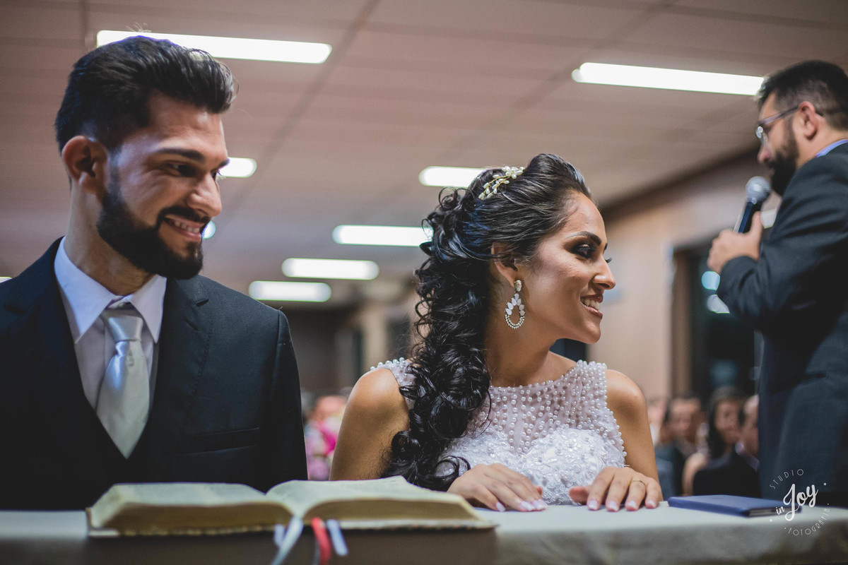 Noivos sorrindo durante a cerimonia de casamento ajoaelhados perto da biblia