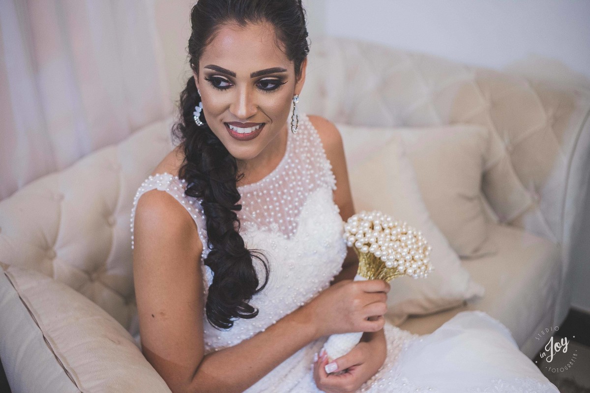Fotografia de noiva sorrindo com o buque sentada em um sofá