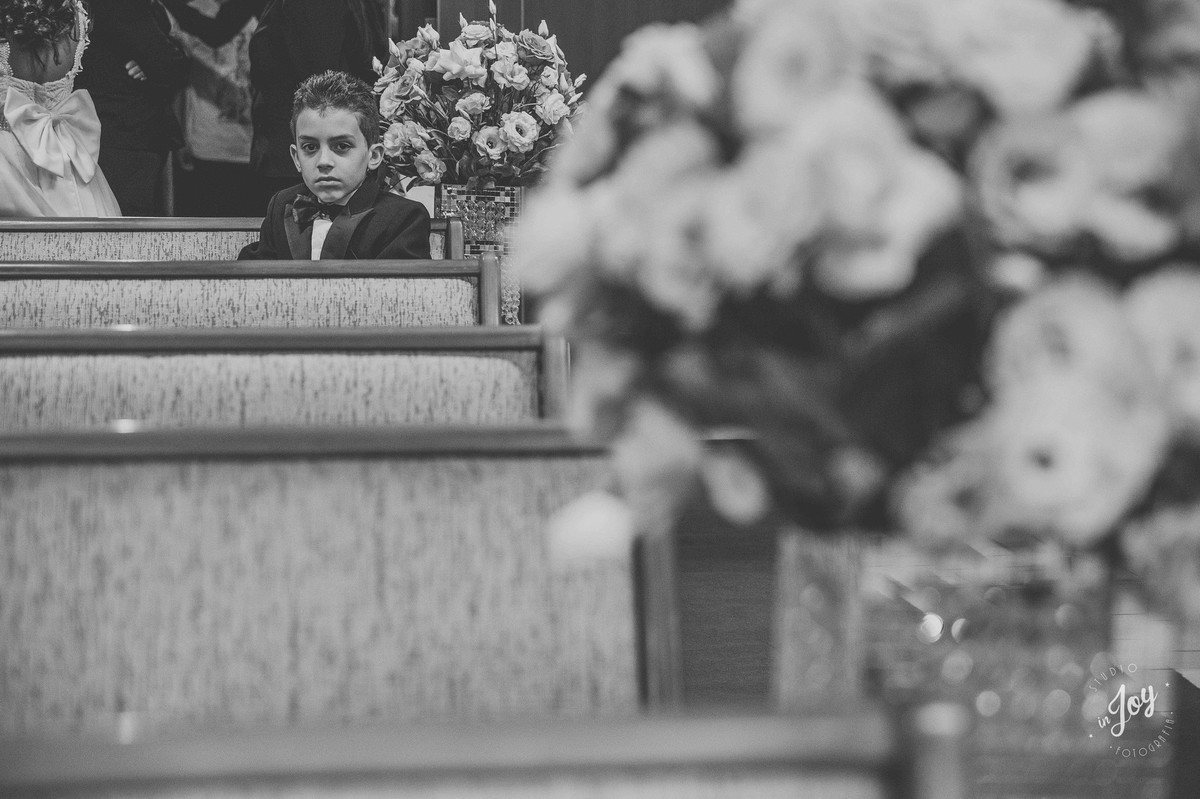 pagem sentado no banco da igreja ao lado de um arranjo de flores e encarando a camera