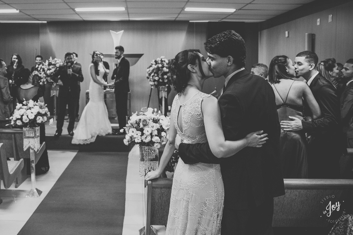 Convidados se beijando durante a cerimonia de casamento e os noivos olhando para eles