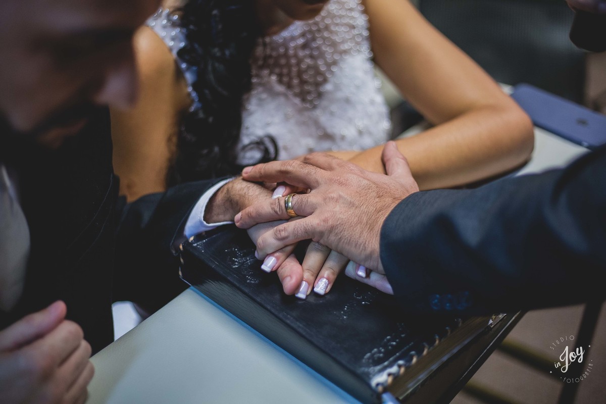 Pastor abençoando os noivo pondo suas mão sobre a mão dos noivos encima da biblia