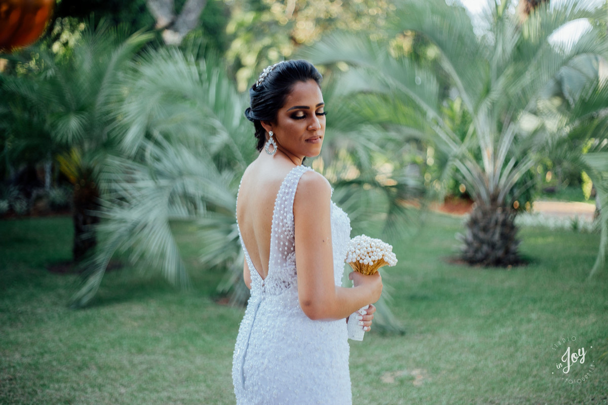 detalhes vestido de noiva sereia com as costas abertas e segurando um boque feito pelo noivo de perolas