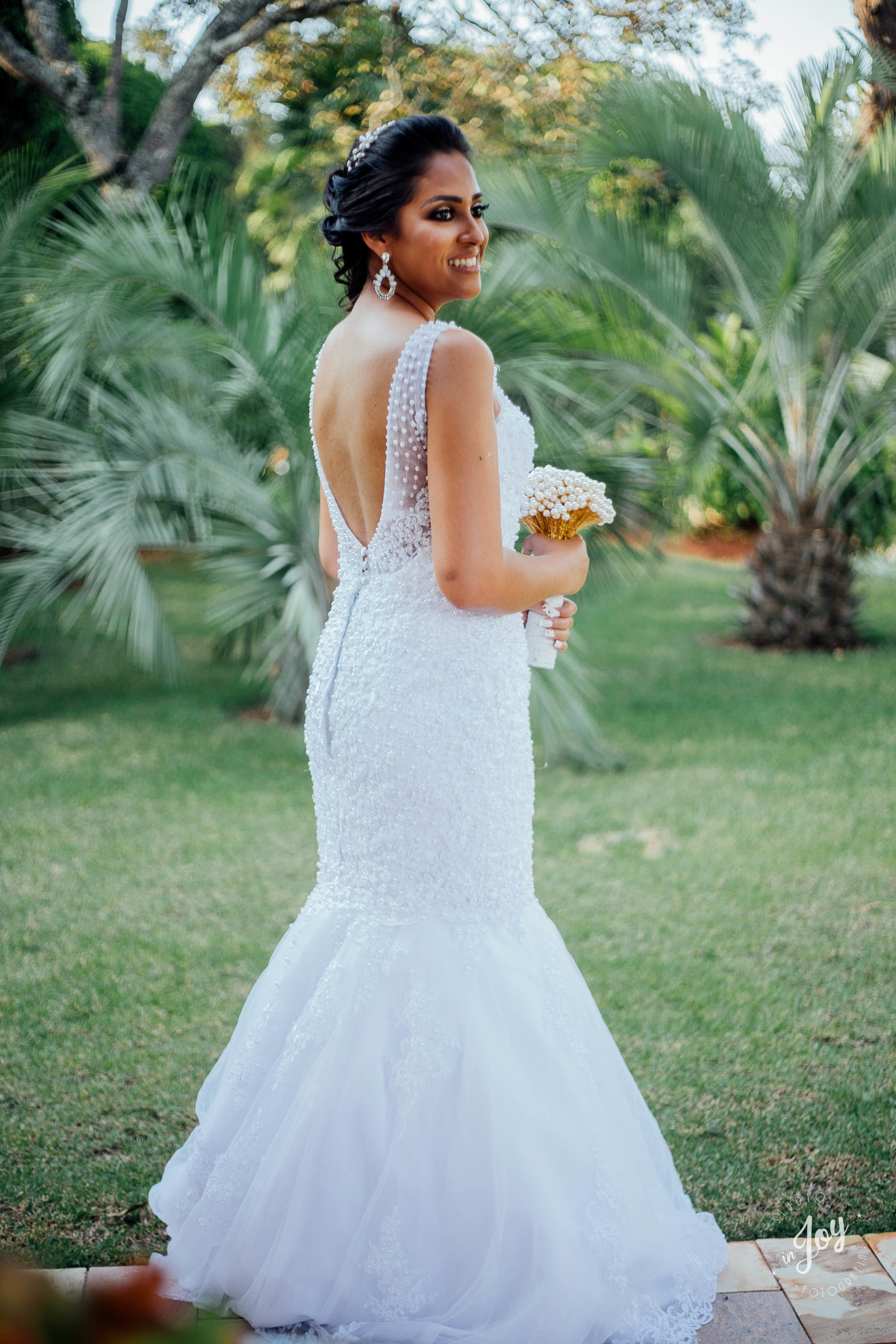 detalhes vestido de noiva sereia com as costas abertas e segurando um boque feito pelo noivo de perolas