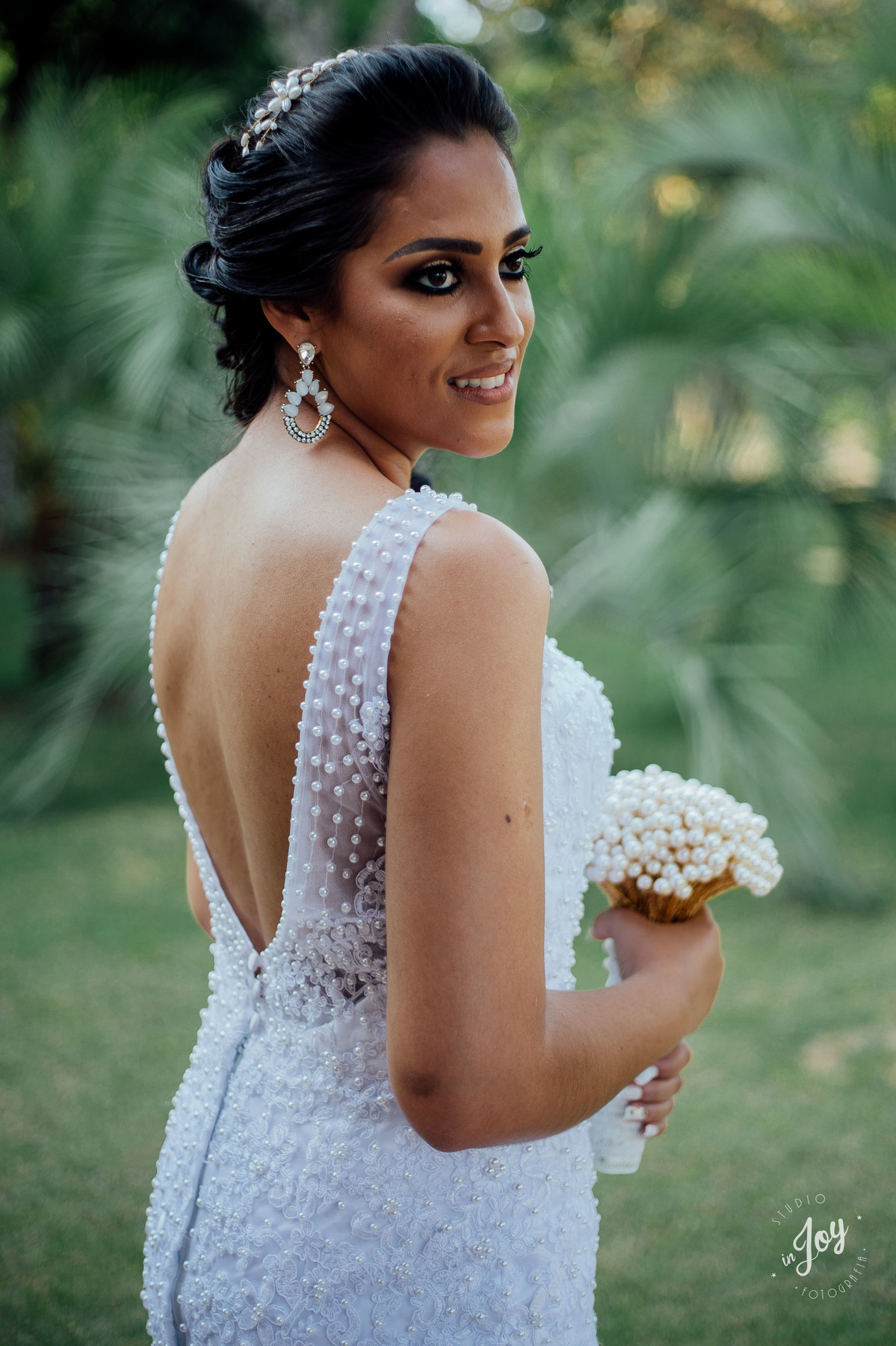 detalhes vestido de noiva sereia com as costas abertas e segurando um boque feito pelo noivo de perolas