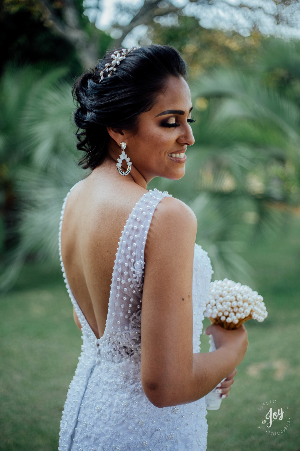 detalhes vestido de noiva sereia com as costas abertas e segurando um boque feito pelo noivo de perolas