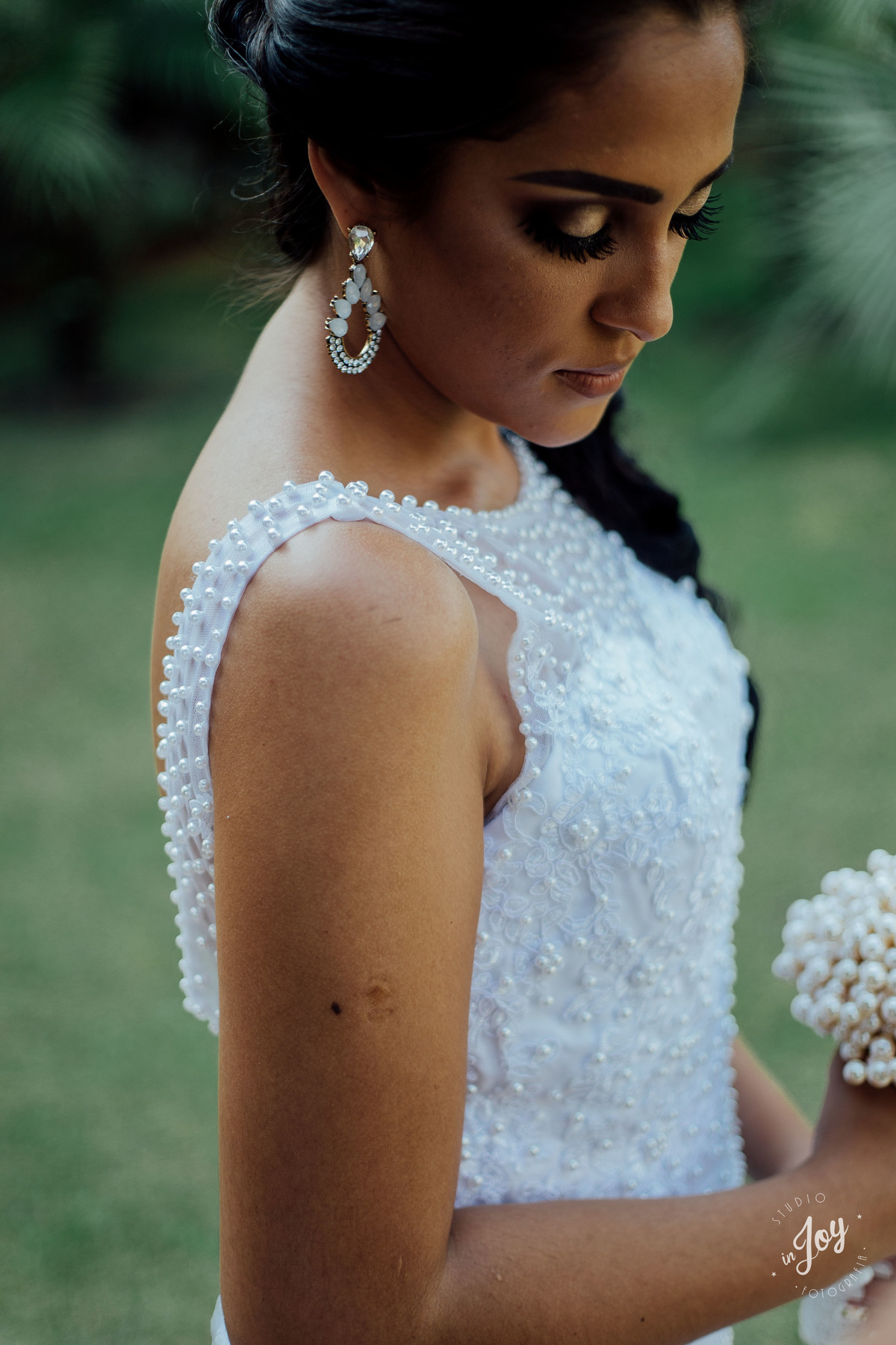 noiva segurando um boque feito pelo noivo de perolas e mostrando detalhes do vestido e dos brincos para casamento