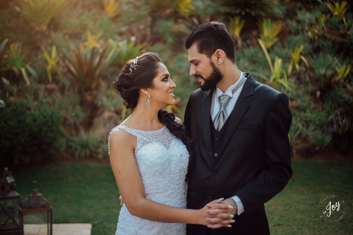 Noivos se olhando e de mãos dadas sorrindo em um por do sol