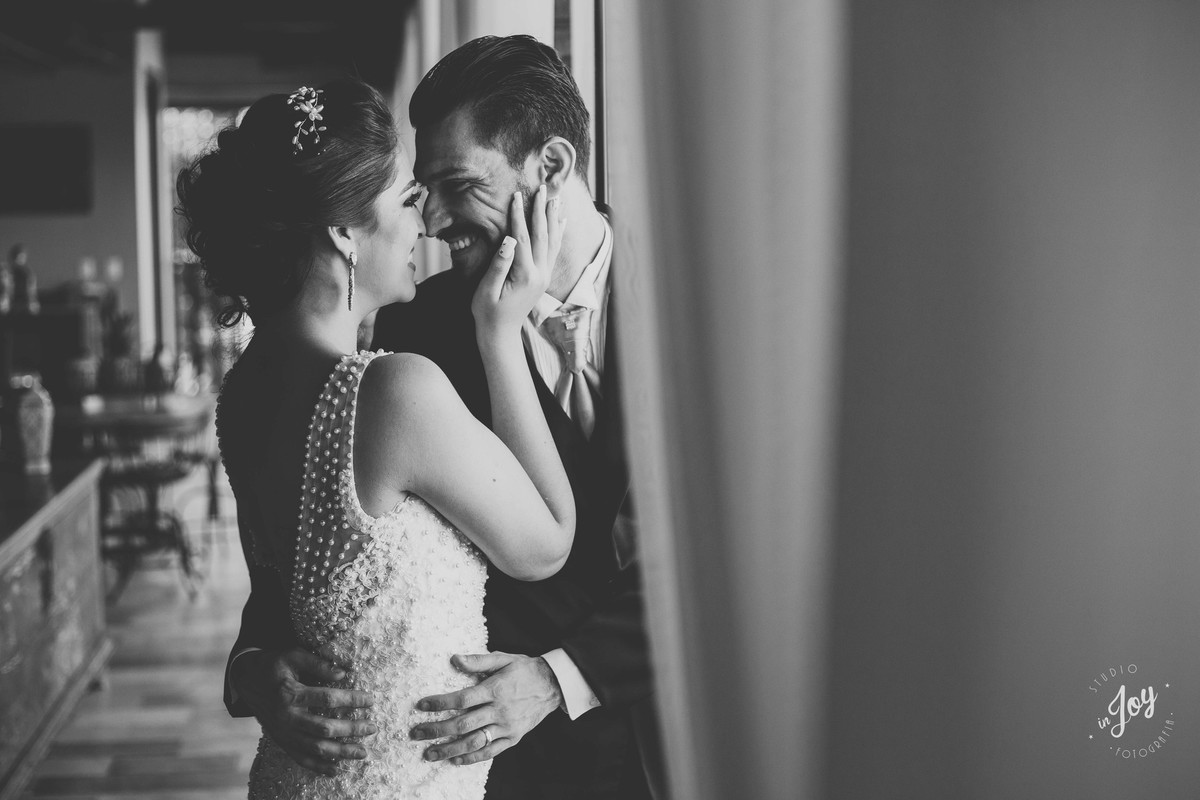 noivos sorrindo e se abraçando perto da janela durante o ensaio de pós casamento