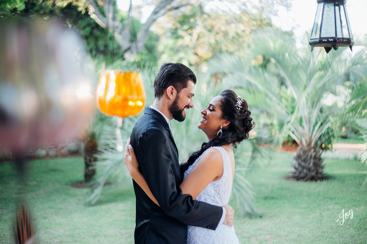 fotografia de pós casamento noivos se abraçando e sorrindo um pro outro em um jardim muito bonito e com luminarias