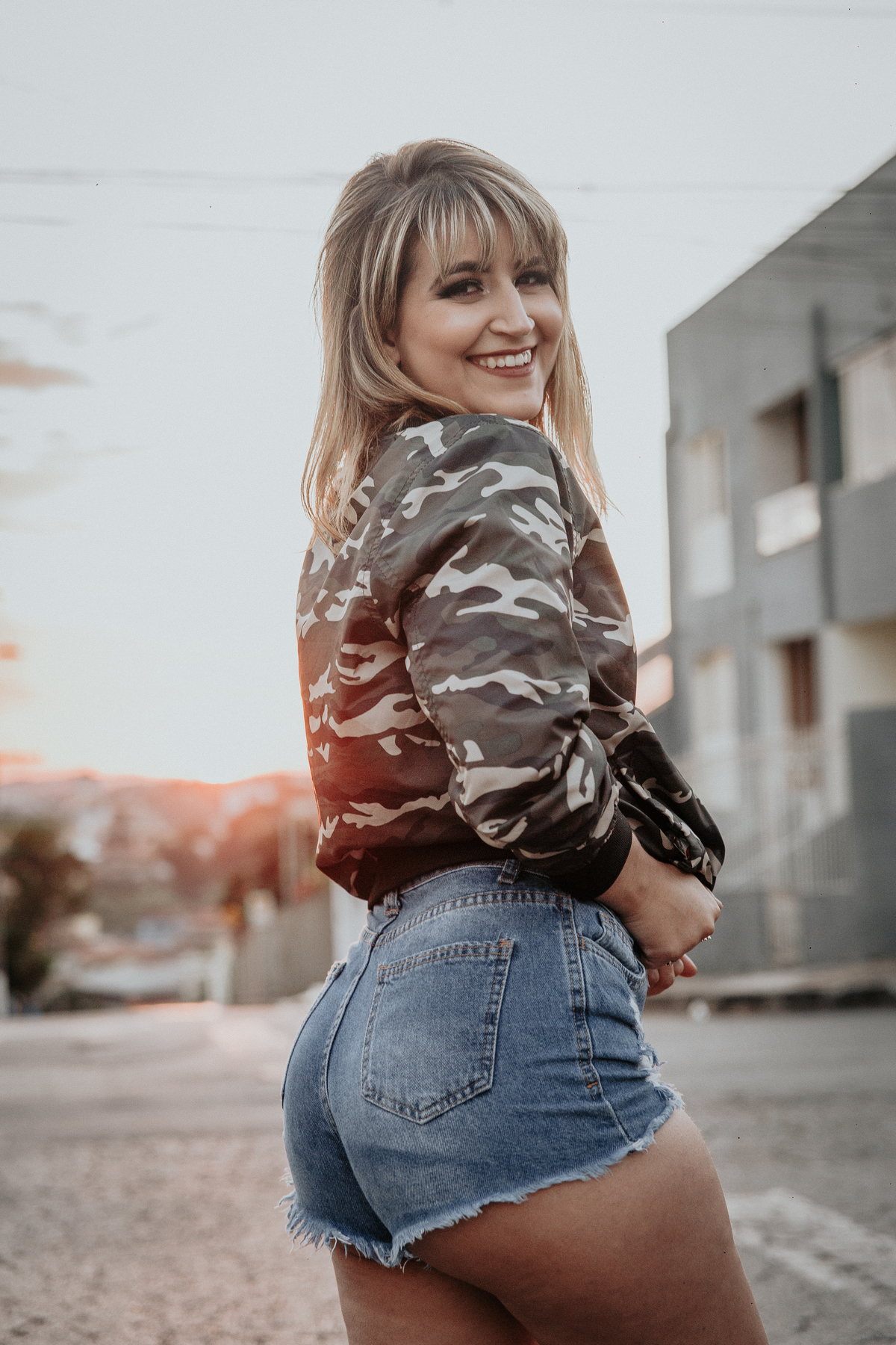 ensaio feminino em betim dentro do carro com uma inspiração de look com jaqueta corta vento camuflada e short jeans com tenis fila branco