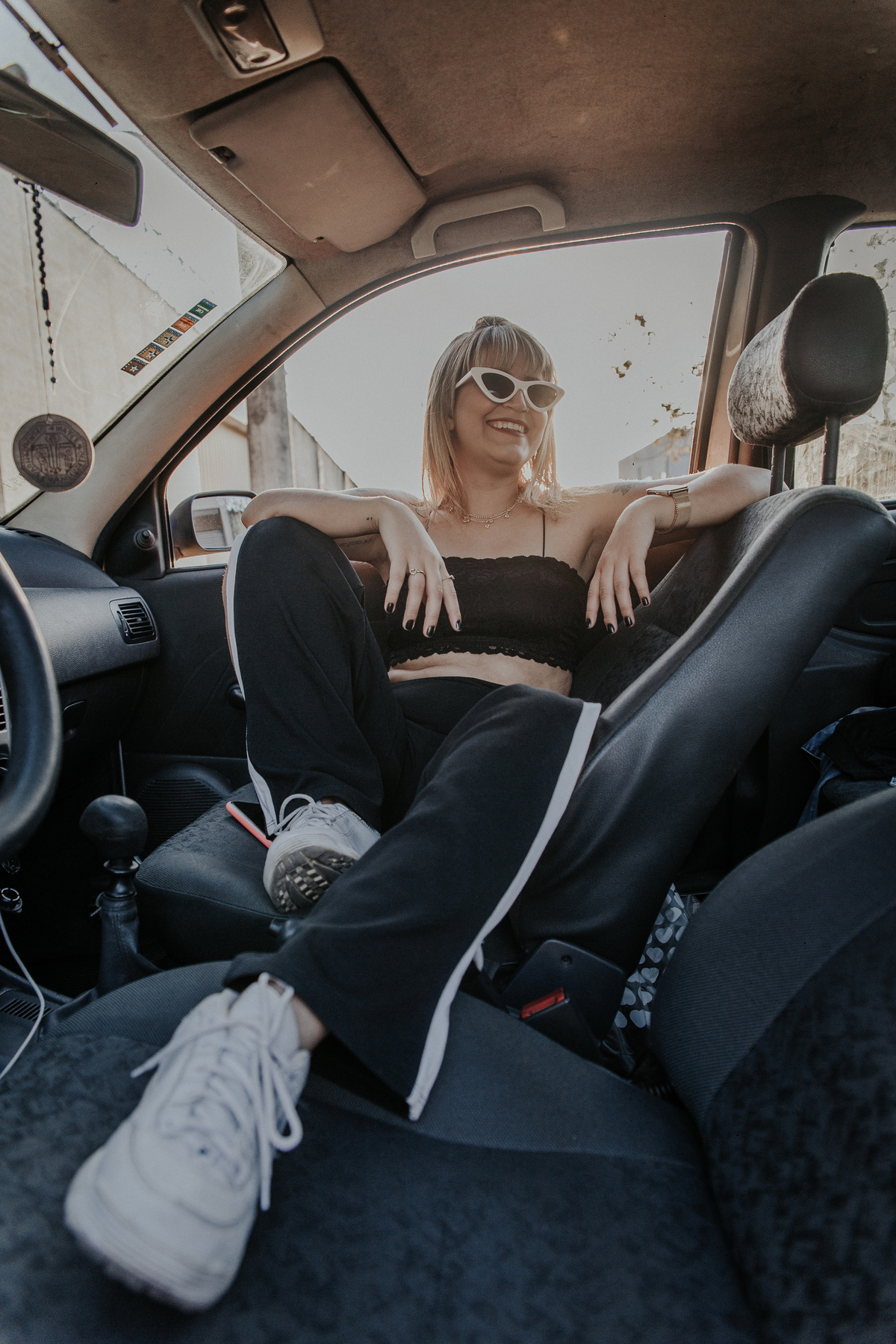 ensaio feminino em betim dentro do carro com uma inspiração de look com jaqueta corta vento, calça pantalona e oculos de sol retro