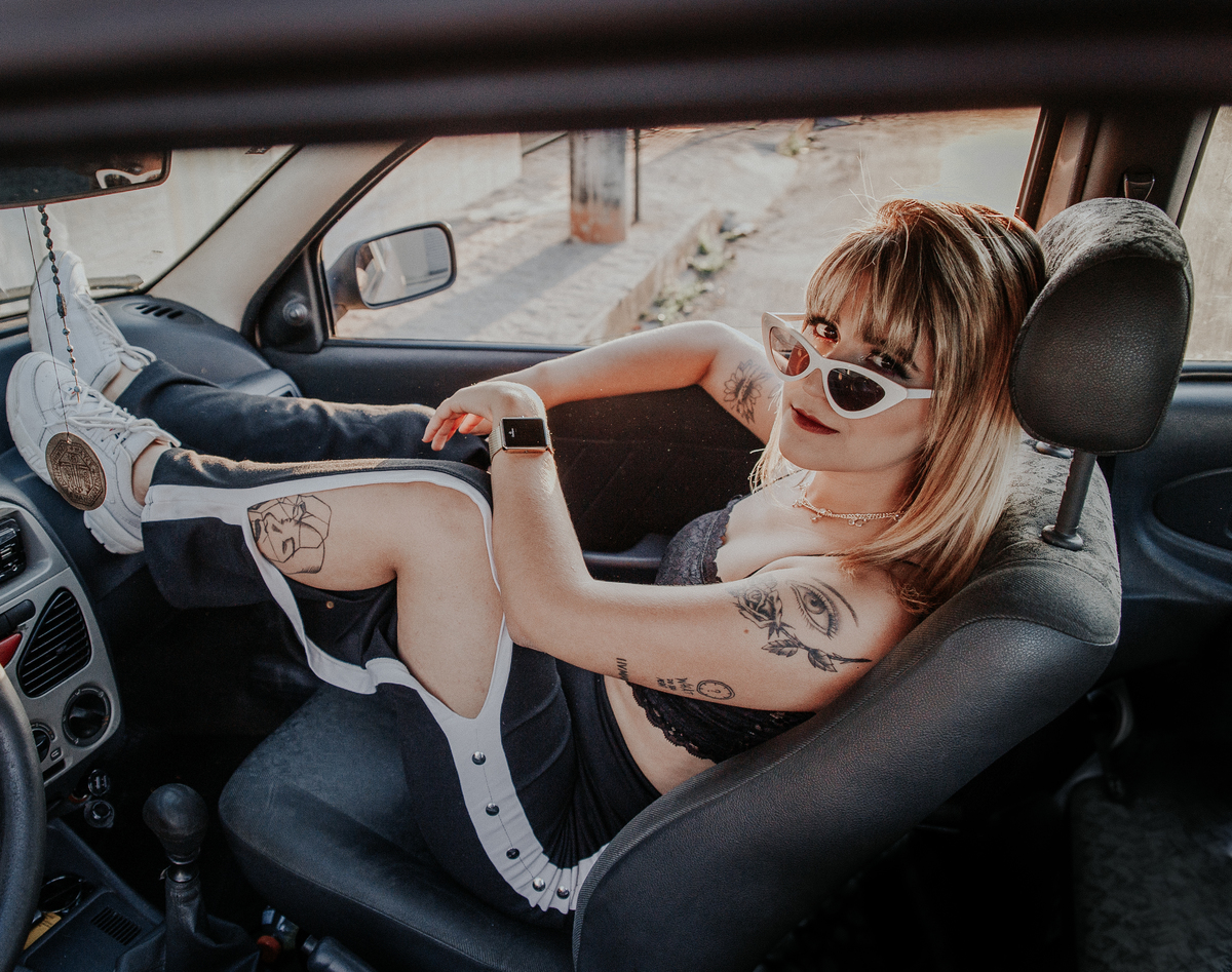 ensaio feminino em betim dentro do carro com uma inspiração de look com jaqueta corta vento, calça pantalona e oculos de sol retro
