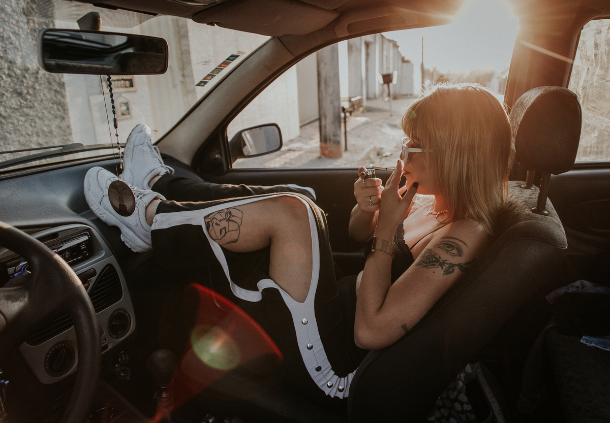 ensaio feminino em betim dentro do carro com uma inspiração de look com jaqueta corta vento, calça pantalona e oculos de sol retro
