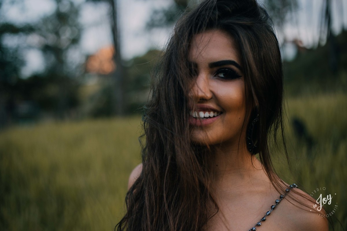 Modelo sorrindo para a camera enquanto um vento bate em seus cabelos