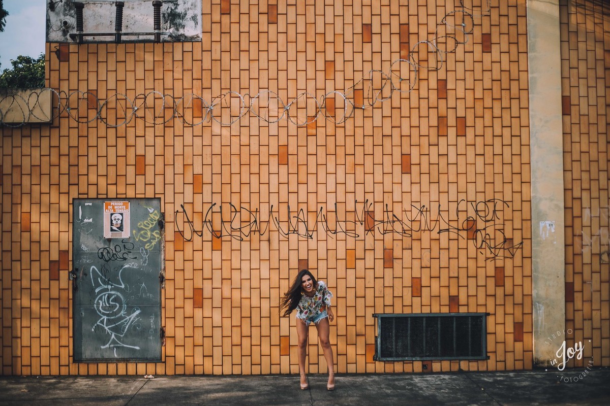 modelo sorrindo em um ensaio fotográfico divertido em Betim Minas Gerais na frente de uma parede de tijolinhos