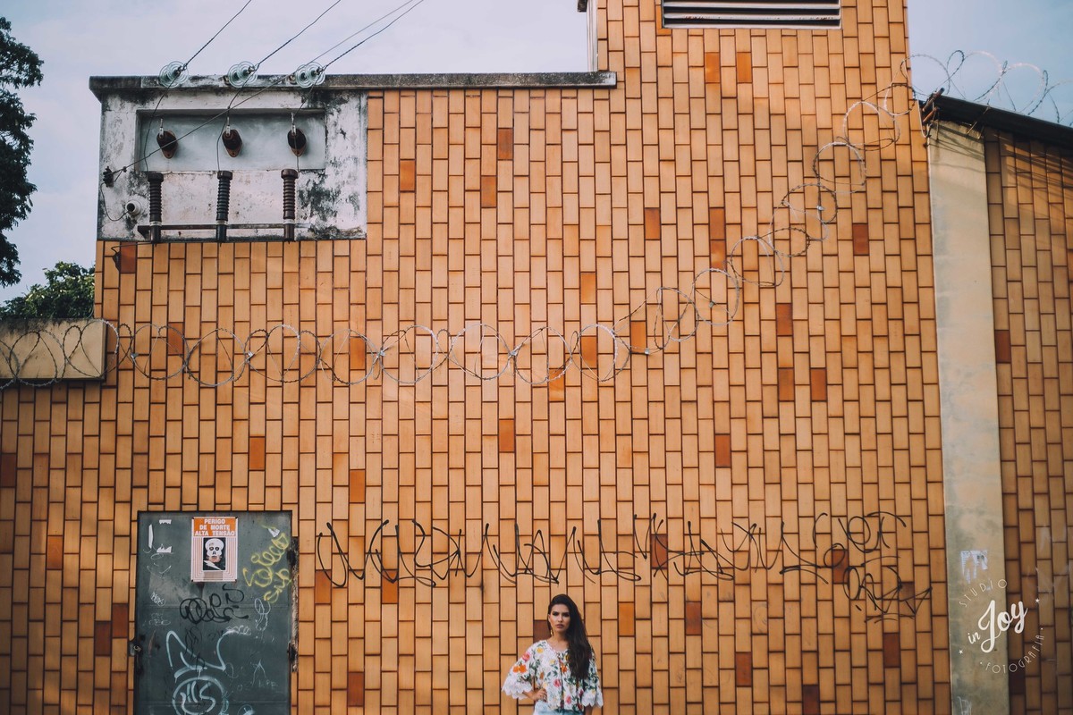 Alicia Bethania posando na frente de uma parede de tijolinhos e olhando para a camera em um ensaio fotográfico feminino em Betim