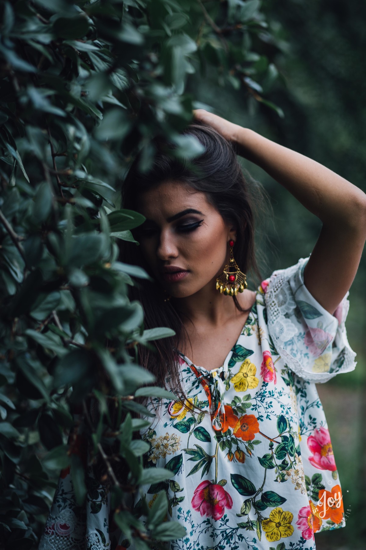 Modelo segurando o cabelo e com os olhos fechados escorada em um muro de trepadeiras