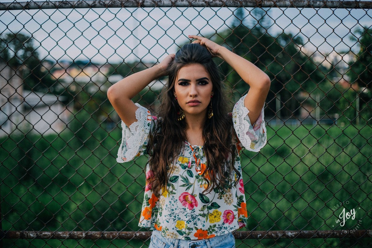 Fotografia Alicia Bethania em Betim na frente de uma cerca de tela formando uma fotografia criativa e espontanea