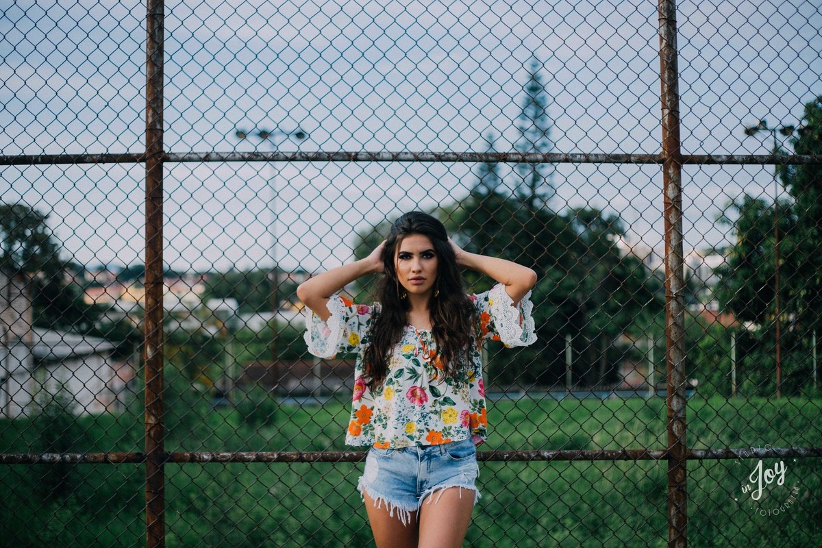 Fotografia Alicia Bethania em Betim na frente de uma cerca de tela formando uma fotografia criativa e espontanea