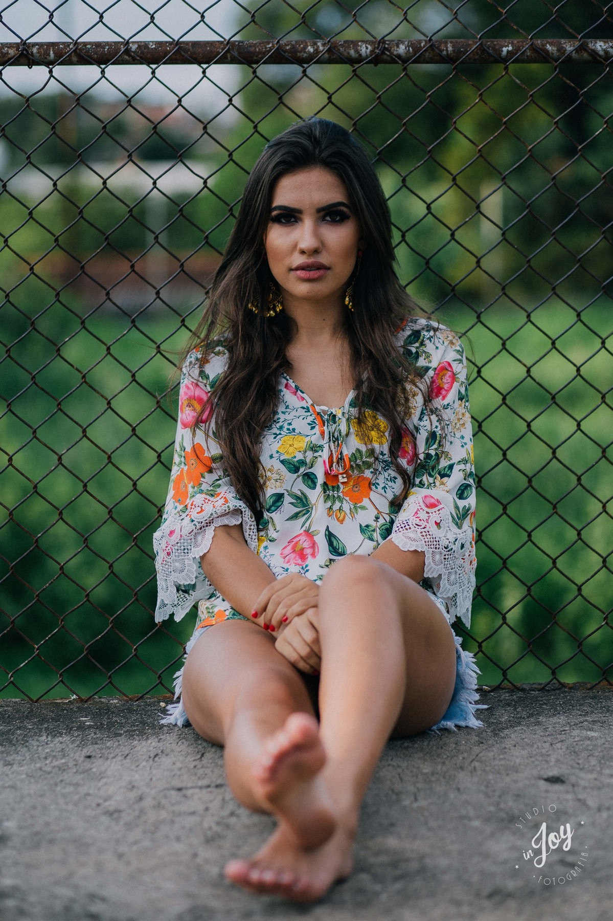 modelo sentada olhando para a camera escorada em uma cerca de talas com uma blusa flora e short curto