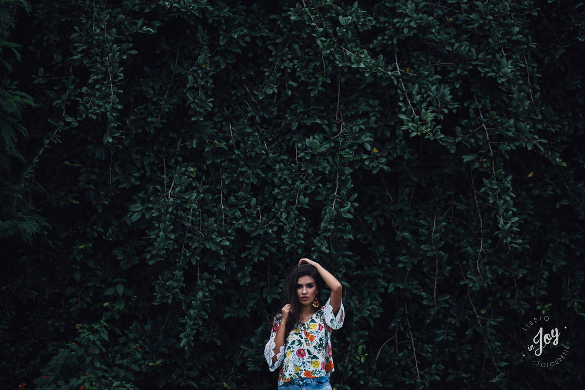 fotografia de moda em que a modelo está na frente de uma trepadeira verde e segurando o cabelo com uma blusa floral