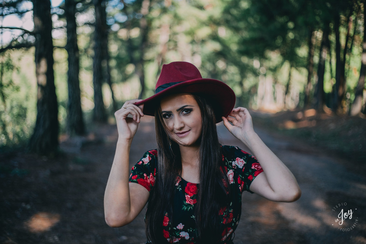 Ensaio feminino em que a modelo esta serando a aba de um chapéu vermelho