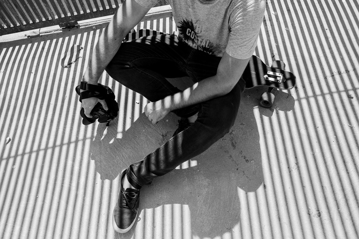 Fotografia PeB em Betim em que o modelo esta sentado encima de um longboard e segurando uma camera fotografica